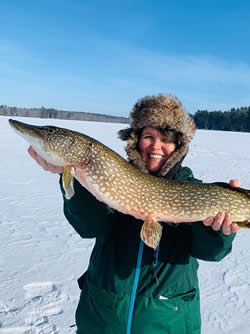Smiling woman holding a very large Northern Pike she caught ice fishing.