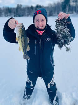 Woman, standing in snow, showing the Largemouth Bass she caught.