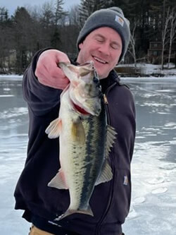 Man standing on a frozen lake holding a Largemouth Bass he caught.