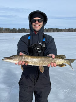 Man holding a Northern Pike he caught ice fishing.