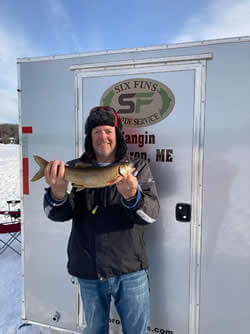 Man standing by Six Fins Guide Service trailer with his Lake Trout.