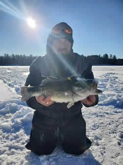 Man kneeling on the ice holding a Largemouth Bass.