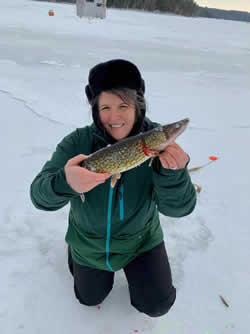 Woman kneeling on the ice holding a Chain Pickerel.