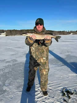 Man standing on a frozen lake holding a Northern Pike he caught.