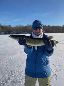Woman, bundled in winter geer holding a large Chain Pickerel she caught.