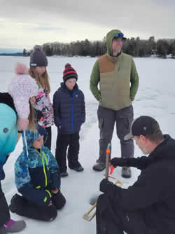 Family group of adults and children learning about ice fishing.