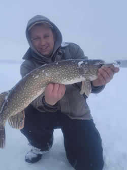 Man kneeling on ice holding a large Northern Pike.