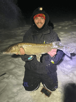 Evening photo of a smiling man holding a Northern Pike.